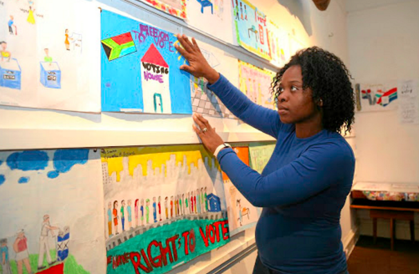 A teacher hangs up pictures her students have made that say "freedom to vote"