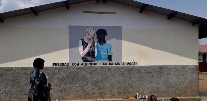 A painting on a wall depicting a white and a black boy with the caption, "People with albinism are the same as you"