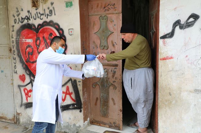 A doctor hands some groceries to a man outside of his house