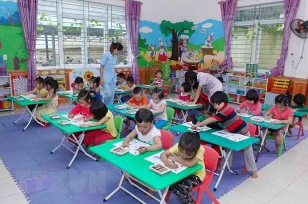 A classroom of children learns by coloring while teachers walk around helping them